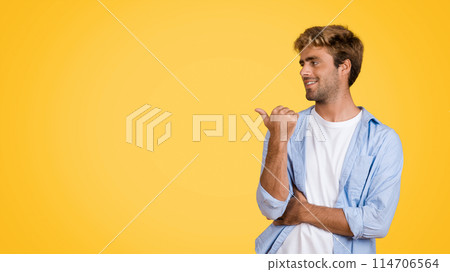 Happy European man stands against bright yellow studio backdrop, smiling and pointing to free space, perfect for an advertisement or showcasing design concept Happy European man stands against bright yellow studio backdrop, smiling and pointing to free space, perfect for an advertisement or showcasing design concept 114706564