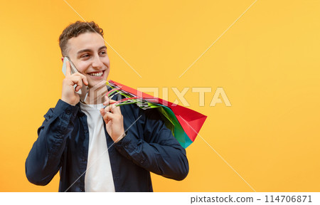 Photo portrait of handsome young guy hold shopping bags packages talking phone wear trendy casual clothes isolated on yellow color background, panorama with copy space 114706871
