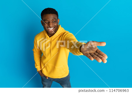 Happy handsome stylish millennial black guy in yellow hoodie holding something invisible on his palm, showing blank space on yellow background, recommending good or service, high angle view Happy handsome stylish millennial black guy in yellow hoodie holding something invisible on his palm, showing blank space on yellow background, recommending good or service, high angle view 114706963