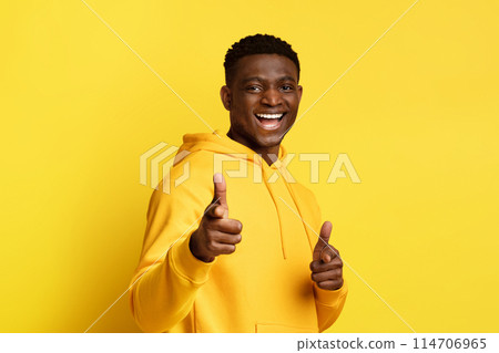 Cheerful cool handsome millennial african american guy wearing yellow hoodie gesturing, pointing with both hands and smiling at camera, isolated on yellow studio background Cheerful cool handsome millennial african american guy wearing yellow hoodie gesturing, pointing with both hands and smiling at camera, isolated on yellow studio background 114706965