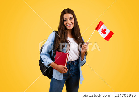Happy caucasian teenager student woman, with Canada flag and book, enjoy exchange study, isolated on yellow background. Lifestyle, national pride and learning English, French 114706989