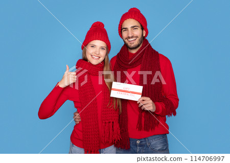 Smiling Young Couple Wearing Knitted Hats Holding Gift Certificate And Showing Thumb Up At Camera, Happy Millennial Man And Woman Advertising Christmas Holiday Sales, Standing On Blue Background Smiling Young Couple Wearing Knitted Hats Holding Gift Certificate And Showing Thumb Up At Camera, Happy Millennial Man And Woman Advertising Christmas Holiday Sales, Standing On Blue Background 114706997