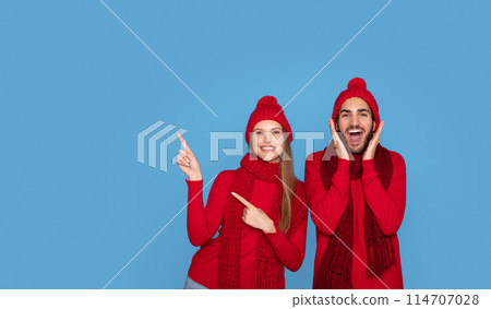 Winter Sale. Excited Young Couple Wearing Knitted Hats Pointing Aside At Copy Space, Cheerful Millennial Man And Woman Demonstrating Free Place On Blue Background, Recommending Xmas Offer, Panorama 114707028
