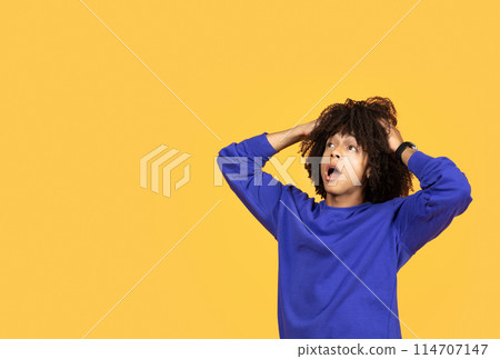 Shocked Black Young Man Opening Mouth And Touching Head While Looking At Copy Space, Surprised Millennial African American Guy Standing Isolated Over Yellow Studio Background, Reacting To Offer 114707147