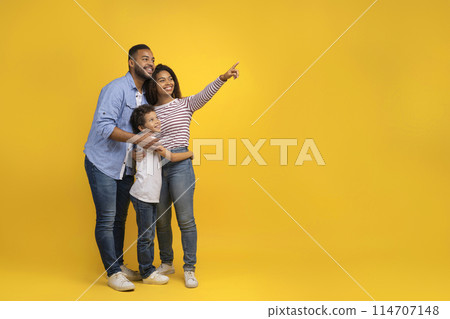 Happy African American Family Of Three Pointing Finger Aside At Copy Space, Young Black Parents And Preteen Son Showing Free Place For Your Text, Posing Together Over Yellow Studio Background 114707148