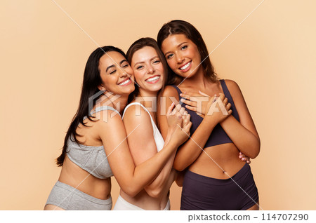 Three joyful international friends in casual underwear embracing and laughing, embodying friendship, diversity, isolated on light background. Lifestyle, body, beauty care Three joyful international friends in casual underwear embracing and laughing, embodying friendship, diversity, isolated on light background. Lifestyle, body, beauty care 114707290