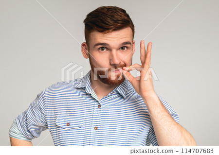 Secret saver. Young guy locking mouth like zip-lock on studio background, panorama, copy space 114707683