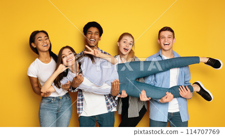 A diverse group of teenagers is seen gathering together and striking various poses in front of a camera, creating a lively and engaging atmosphere, holding their friend A diverse group of teenagers is seen gathering together and striking various poses in front of a camera, creating a lively and engaging atmosphere, holding their friend 114707769