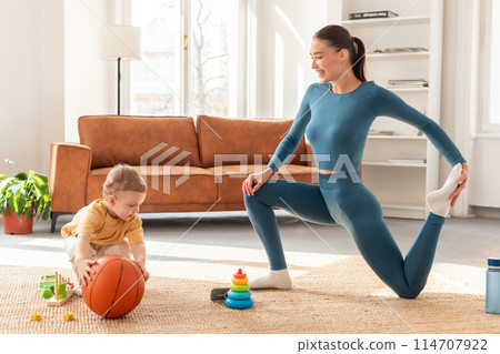 A woman and a child are outdoors, engaging in a game of basketball. The woman is dribbling the ball while the child eagerly attempts to steal it. Both are focused and enjoying the game. 114707922