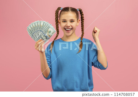 A young girl is seen holding a fan of money in her hand. She looks curious and excited as she grips the bills tightly. 114708057