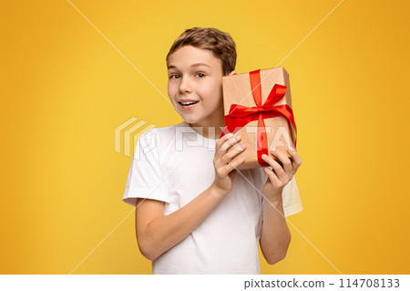 A boy, young in age, holding a wrapped present box in his hands, expressing excitement and anticipation. 114708133