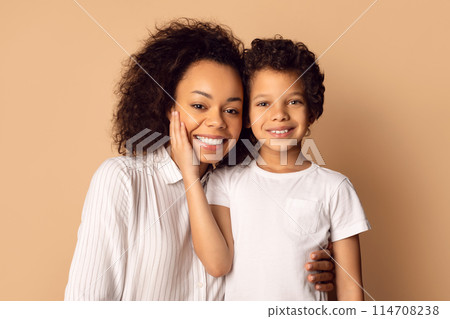 African American woman and a child are standing together, smiling at the camera while posing for a photograph. The woman has her arm around the child in a loving gesture, closeup African American woman and a child are standing together, smiling at the camera while posing for a photograph. The woman has her arm around the child in a loving gesture, closeup 114708238