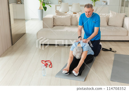 Fitness workout training. Senior adult mature healthy fit couple doing sports exercise on yoga mat at home. Mid age old man trainer helping woman stretching training. Health care healthy lifestyle Fitness workout training. Senior adult mature healthy fit couple doing sports exercise on yoga mat at home. Mid age old man trainer helping woman stretching training. Health care healthy lifestyle 114708352