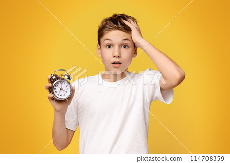 A boy, holding an alarm clock in his hand, looking at the time on the clock. 114708359