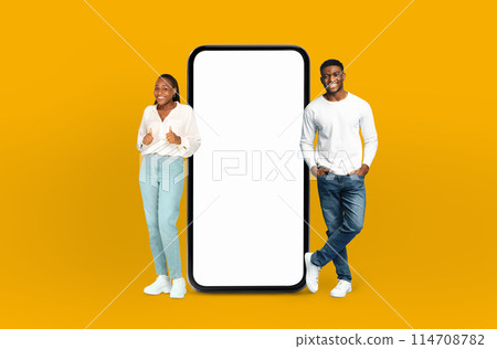 Black man and woman standing next to telephone, appearing to be engaged in a conversation or waiting for a call. They are both looking at the phone, possibly anticipating an important message or call. Black man and woman standing next to telephone, appearing to be engaged in a conversation or waiting for a call. They are both looking at the phone, possibly anticipating an important message or call. 114708782
