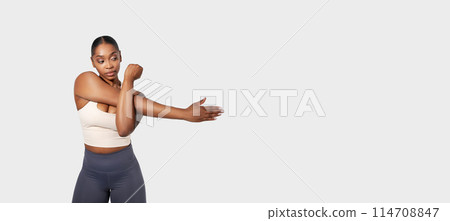 African American woman in the image is flexing her arm, showcasing her muscle definition. The background is plain white, emphasizing the focus on her flexed arm, panorama, copy space 114708847