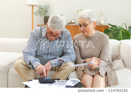 Middle aged senior couple sit with laptop and paper document. Older mature man woman reading paper bill pay online at home managing bank finances calculating taxes planning loan debt pension payment 114709192