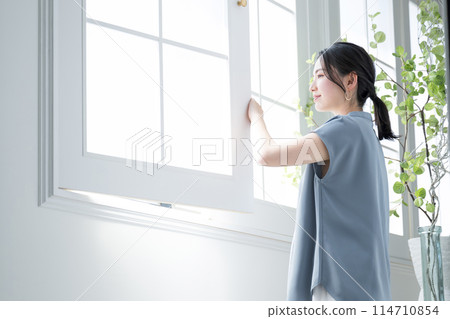 Woman standing by the window, relaxing in the morning sun 114710854