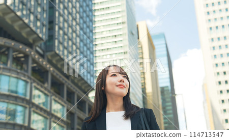 Female business person looking up at the city 114713547
