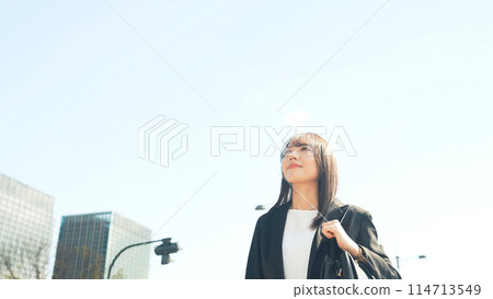 A female business person looking up at the blue sky in the city 114713549