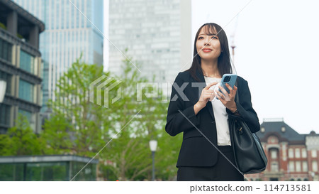 A female business person using a smartphone on a street corner A female business person using a smartphone on a street corner 114713581
