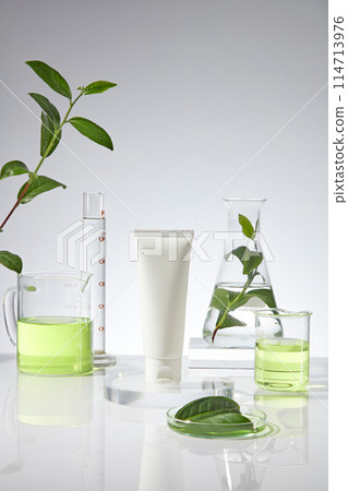 Mock up for advertising with a blank label tube in white color displayed on a glass pedestal in the middle of photo, a beaker, erlenmeyer and measuring cylinder in back over white background 114713976