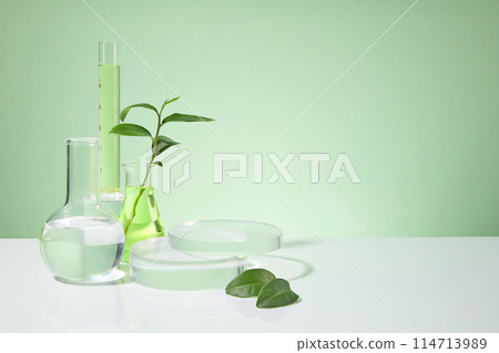 Light green background featured some lab glassware placed on white table top consist of boiling flask, measuring cylinder, erlenmeyer and empty pedestal, the right side is blank for showing product Light green background featured some lab glassware placed on white table top consist of boiling flask, measuring cylinder, erlenmeyer and empty pedestal, the right side is blank for showing product 114713989