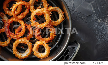 Golden brown onion rings cooked in an air fryer on a dark textured surface Golden brown onion rings cooked in an air fryer on a dark textured surface 114714749
