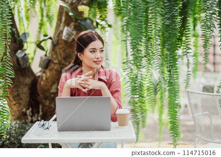 A woman is sitting at a table with a laptop and a cup of coffee. She is wearing a pink shirt and has her hands on her lap. The scene suggests a relaxed and comfortable atmosphere A woman is sitting at a table with a laptop and a cup of coffee. She is wearing a pink shirt and has her hands on her lap. The scene suggests a relaxed and comfortable atmosphere 114715016
