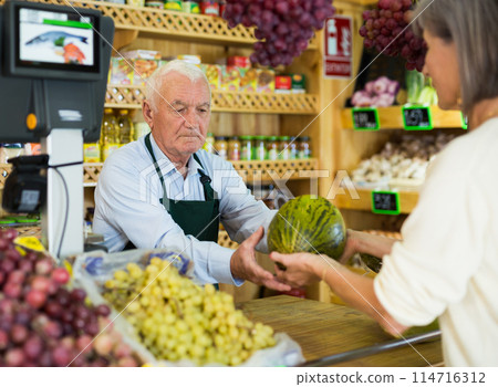 Male grocery store worker handing watermelon to customer after payment at checkout closeup Male grocery store worker handing watermelon to customer after payment at checkout closeup 114716312