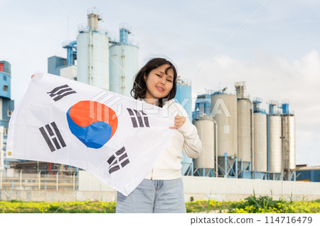 Happy young woman with flag of South Korea against background of factory Happy young woman with flag of South Korea against background of factory 114716479