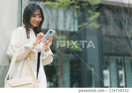 A young woman operating a smartphone in the city 114716552