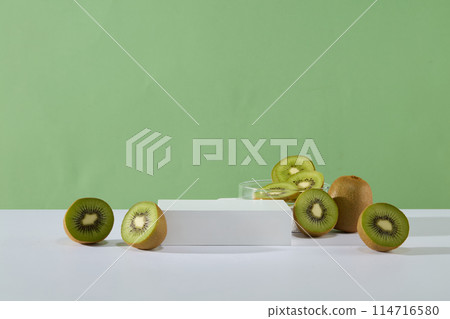 Pastel green background features a petri dish of kiwi slices placed behind an empty podium. Product photography. Kiwis are a delicious and nutritious fruit choice for most people 114716580
