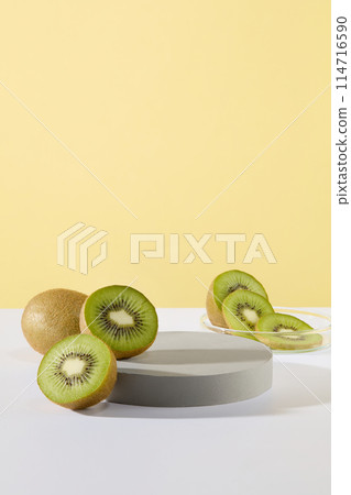 Gray podium in round shaped and some slices and halves of kiwi fruit are featured over pastel color background. Vacant space for presentation. Stage showcase on pedestal display Gray podium in round shaped and some slices and halves of kiwi fruit are featured over pastel color background. Vacant space for presentation. Stage showcase on pedestal display 114716590