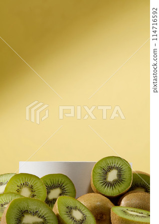 Front view of many kiwi fruit cut in halves surrounded a white podium in cylinder shaped. Minimal background in pastel color. Kiwi fruit is great for both health and skin 114716592