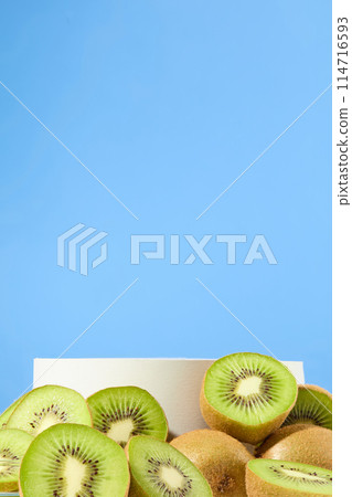 On the light blue background, an empty cylinder podium is surrounded by lots of kiwis. Kiwis contain nutrients that help balance out your sebaceous gland production 114716593