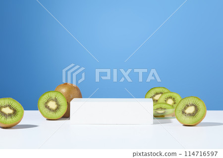 Blue background features a white podium in rectangle shaped with some kiwi halves. Kiwi revitalizes skin by protecting against damage, boosting collagen, and enhancing radiance 114716597