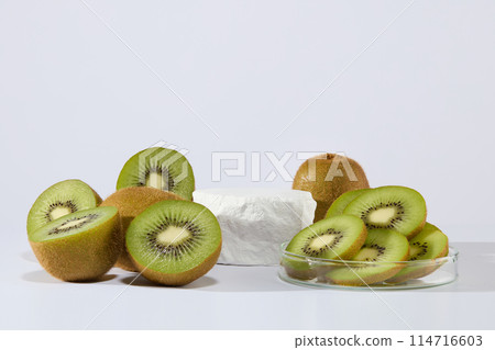 An empty podium is surrounded by lots of fresh kiwi fruit cut in halves and slices. Minimal podium display for cosmetic product presentation. Using kiwi for skin is great way to pamper it 114716603