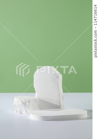 Minimal scene of a white podium decorated with few blocks of stone over green background. Concept scene stage showcase for new product, promotion sale, cosmetic presentation 114716614