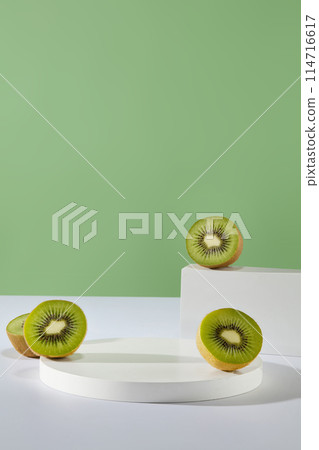 Delicious kiwi fruit cut in halves are placed on some empty pedestals. Green background. Blank space for product advertisement. Kiwi is associated with a variety of health benefits Delicious kiwi fruit cut in halves are placed on some empty pedestals. Green background. Blank space for product advertisement. Kiwi is associated with a variety of health benefits 114716617