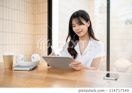 A beautiful Asian businesswoman is working on her digital tablet, writing with a stylus pen. 114717349