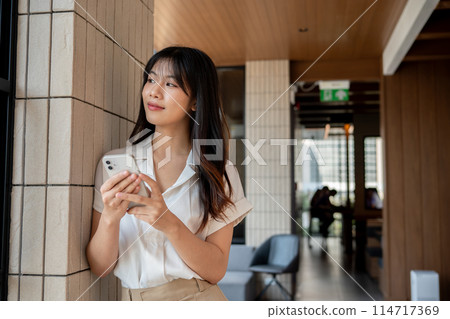 A businesswoman leans against the wall in the company's hallway, looking away from the camera. A businesswoman leans against the wall in the company's hallway, looking away from the camera. 114717369