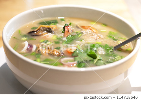Boiled rice soup with squid, mussels and shrimp in white bowl. Asian breakfast style. Seafood Porridge. 114718640