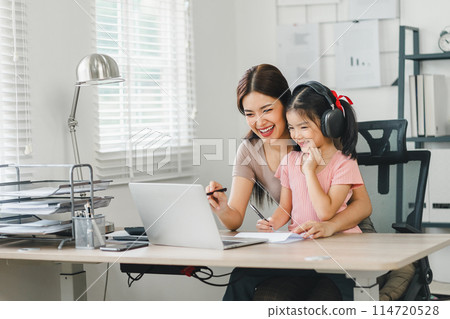Smiling mother and daughter enjoying online communication together at home office. 114720528