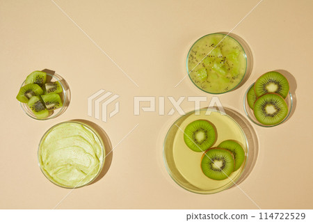 Kiwi is cut into slices or crushed and placed on glass dishes of different sizes over light yellow background. Blank space for designing kiwi exfoliation cream advertising, high angle shot Kiwi is cut into slices or crushed and placed on glass dishes of different sizes over light yellow background. Blank space for designing kiwi exfoliation cream advertising, high angle shot 114722529