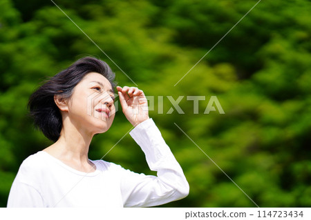 A middle-aged woman standing in the sunlight among the greenery 114723434