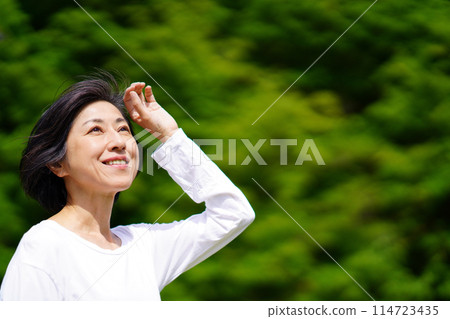 A middle-aged woman standing in the sunlight among the greenery A middle-aged woman standing in the sunlight among the greenery 114723435