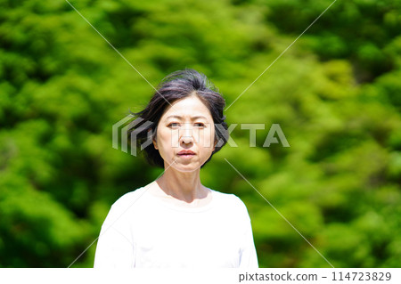 A middle-aged woman wearing white clothes standing lonely among the greenery 114723829