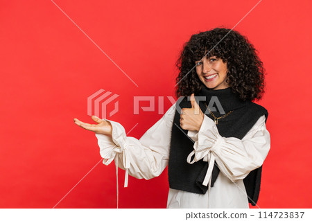 Young woman showing thumbs up and pointing at left on blank space place for your advertisement logo 114723837