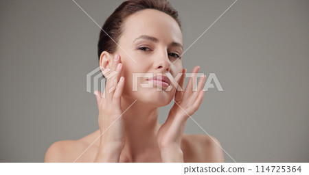 Beauty, health, cosmetics, anti-aging therapy and skin care concept - young beautiful brunette Caucasian woman touching her face skin with her hands, posing and looking at the camera as in a mirror Beauty, health, cosmetics, anti-aging therapy and skin care concept - young beautiful brunette Caucasian woman touching her face skin with her hands, posing and looking at the camera as in a mirror 114725364